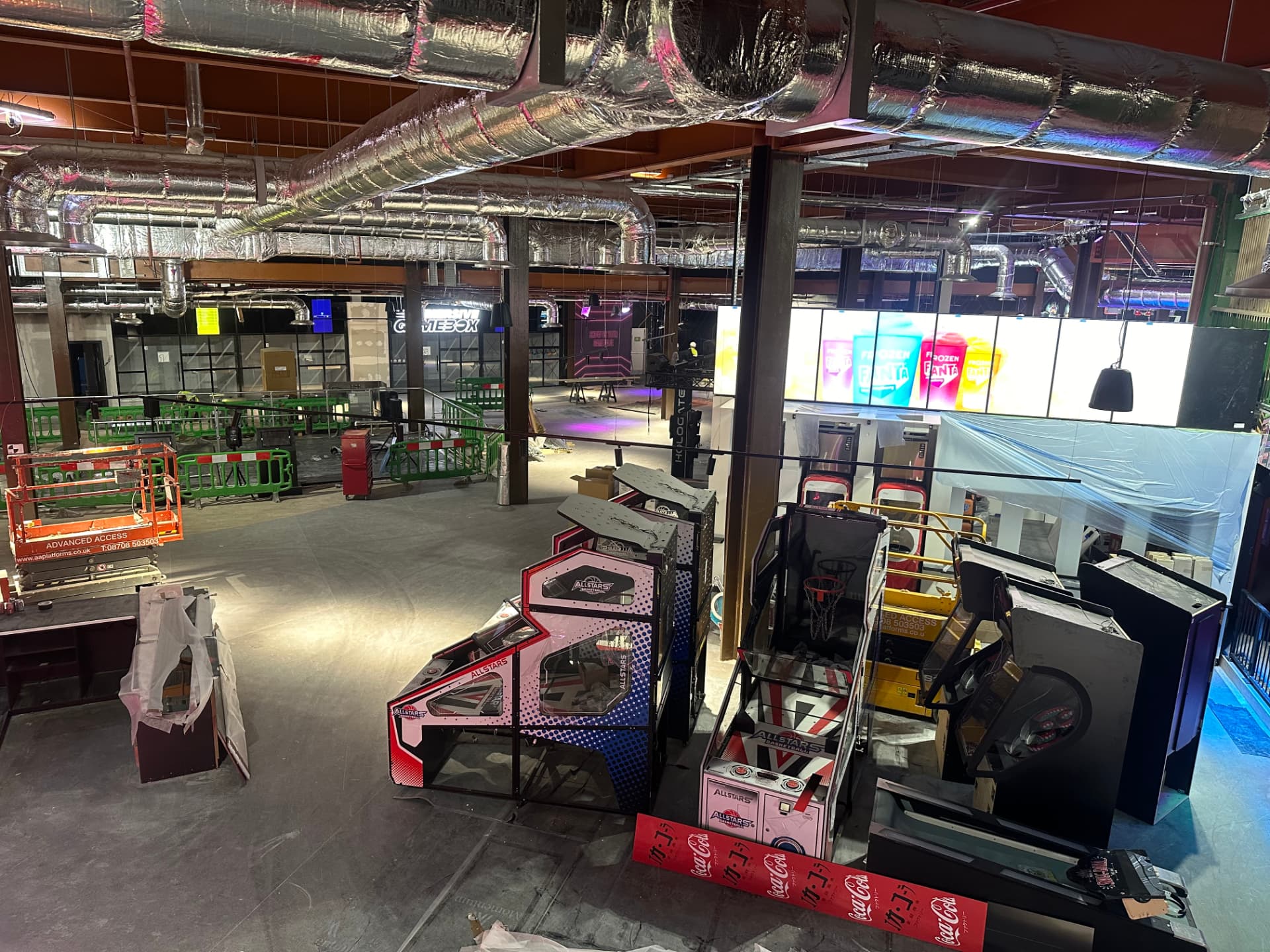 High level view across an arcade floor with illuminated game machines and exposed services overhead