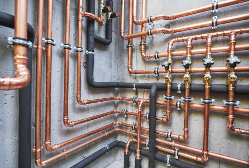 Copper pipework with isolation valves, secure brackets and insulated pipe sections against a concrete wall