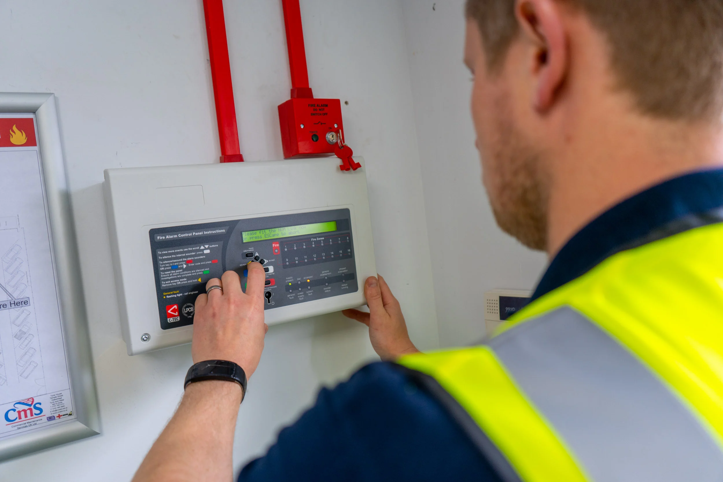 Engineer commissioning a commercial fire alarm control panel beside red fire-rated conduit
