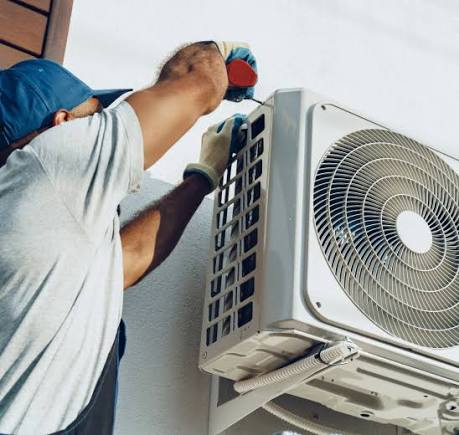 Technician using a hand tool to install an outdoor air conditioning condenser unit on a wall bracket